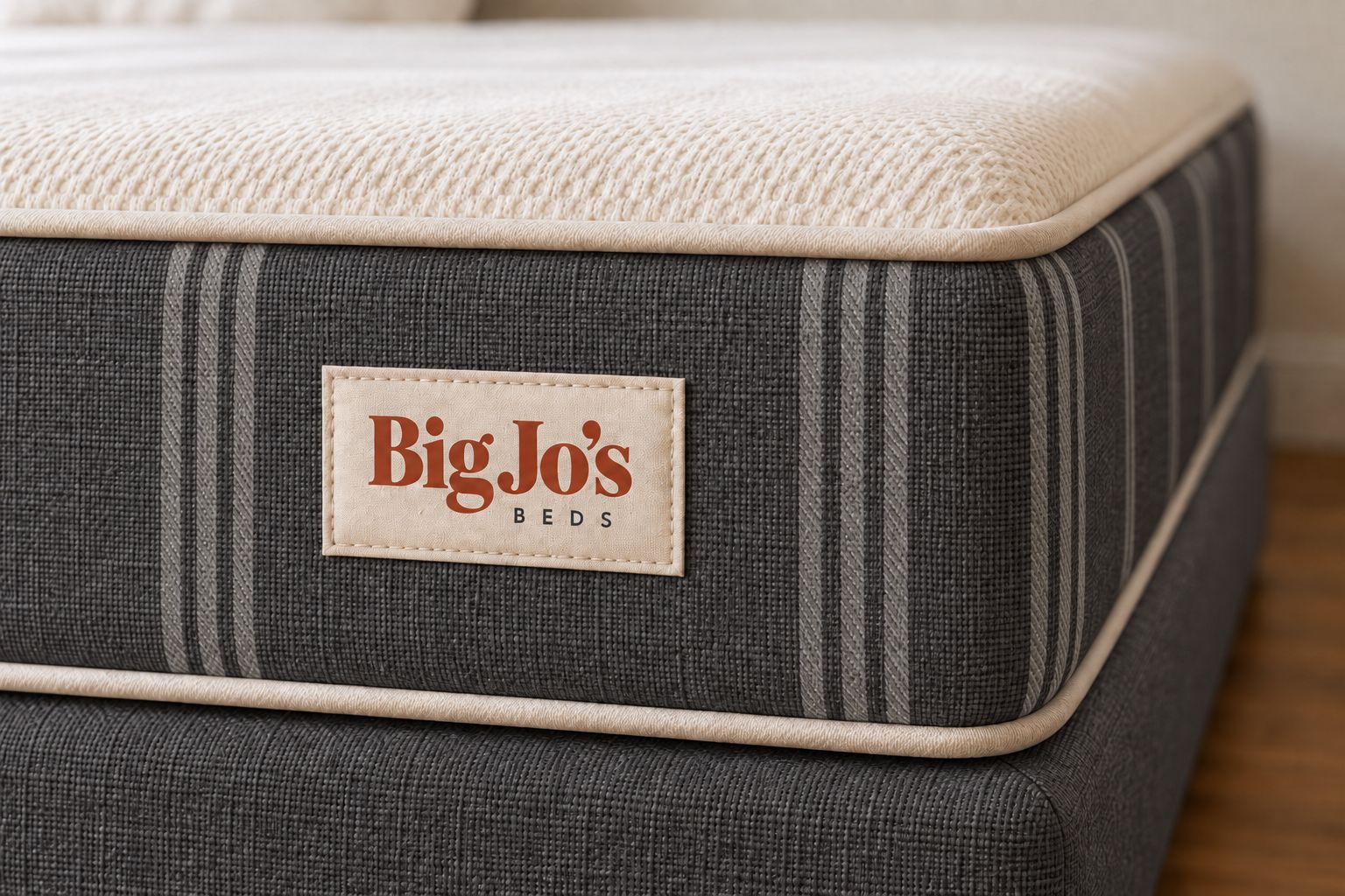 Close-up of the Charcoal finish: dark grey woven fabric, tonal ticking stripes, cream piping and the sewn-on Big Jo’s Beds label.